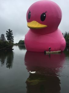 巨大ラバーダッキーとその前を颯爽と泳ぐアヒルさんの画像