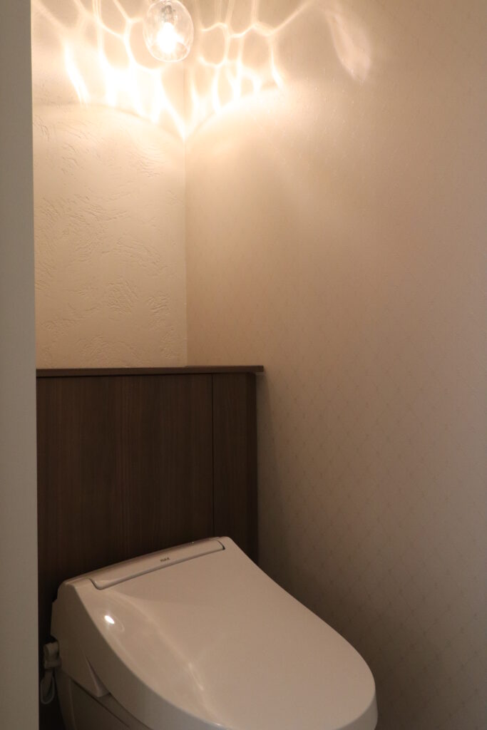 天井に波紋のような陰影が広がるペンダントライトとダークブラウンのタンクレス風収納トイレの画像