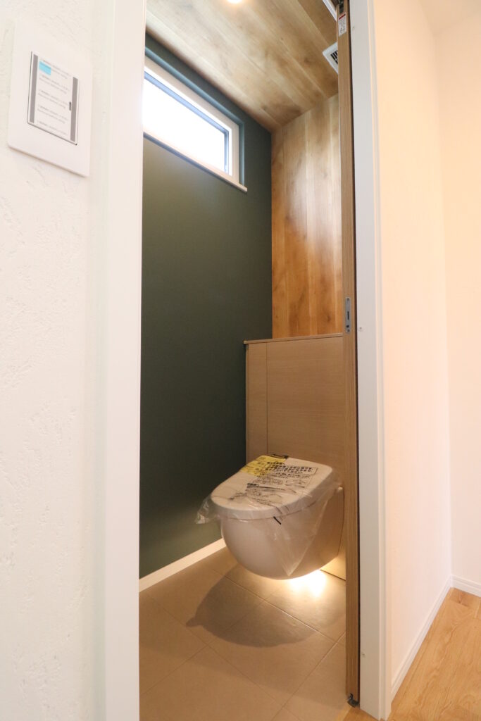 ディープグリーンのアクセントクロスと浮遊感のあるフロートトイレの画像