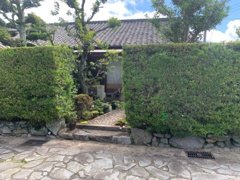 生垣の切れ目から前庭が覗く。鉢植えや室外機——「暮らし」がそこにあるの画像